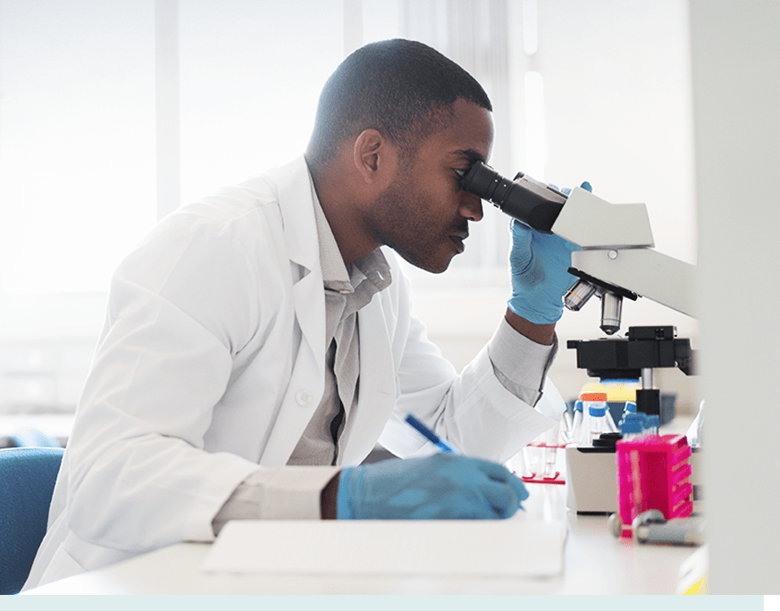 Scientist looking into microscope and writing in notepad