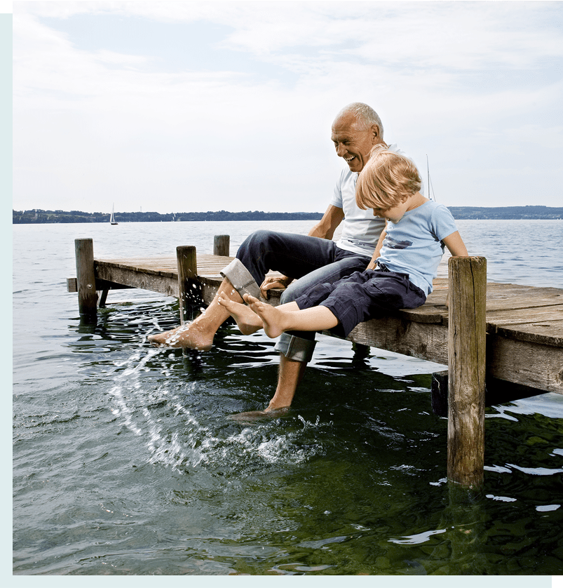 Grandfather and grandson sitting on dock and splashing feet in water